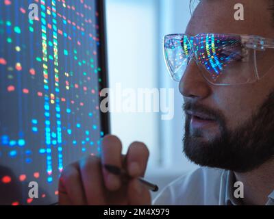 Scientist wearing protective eyeglasses analyzing DNA data on computer in laboratory Stock Photo