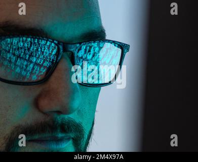 Hacker wearing eyeglasses with reflection of binary codes Stock Photo