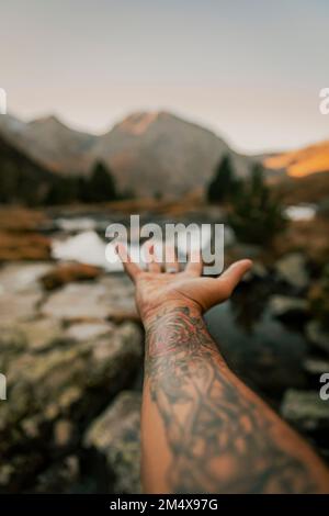 Man with tattooed hand gesturing towards lake Stock Photo