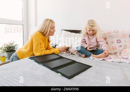 Smiling mother using tablet PC with solar battery charger on bed Stock Photo