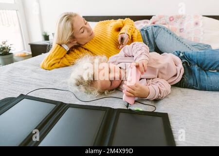 Mother and daughter using smart phones lying on bed Stock Photo