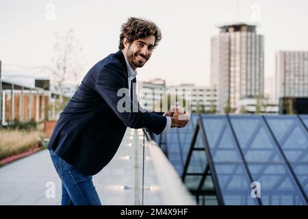 Smiling young businessman leaning on railing Stock Photo