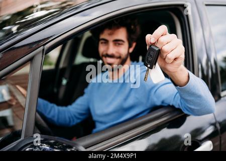 Young man showing key sitting in car Stock Photo