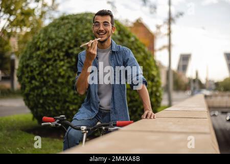 Cheerful young man talking on speaker phone by wall Stock Photo