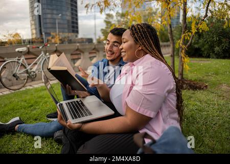 Happy young couple reading book together on grass Stock Photo