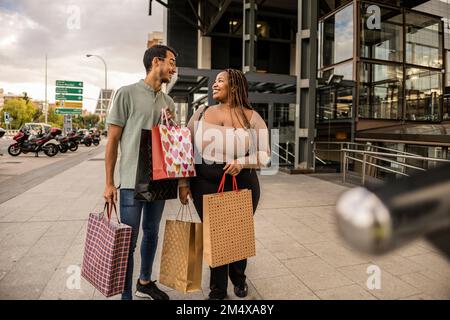 Happy young couple standing with shopping bags on footpath Stock Photo