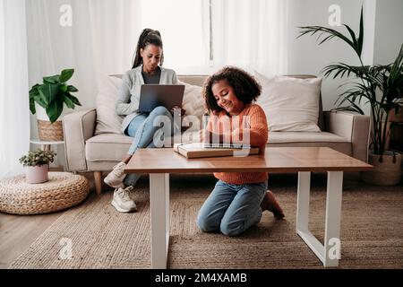 Happy girl doing homework with mother using laptop on sofa at home Stock Photo