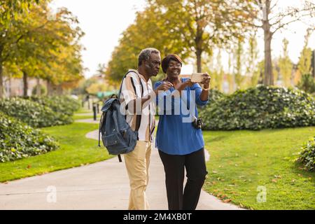 Senior couple using mobile phone standing in park Stock Photo
