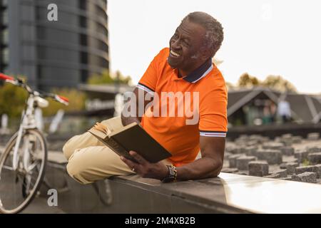 Happy man with book lying on wall Stock Photo