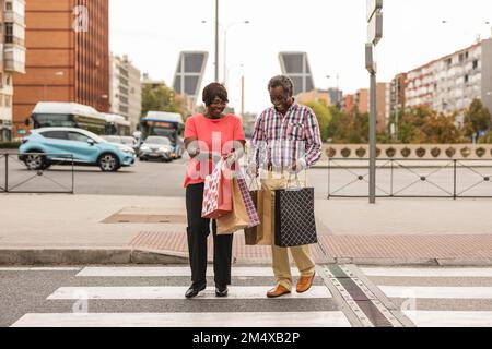 Happy couple with shopping bags crossing road in city Stock Photo