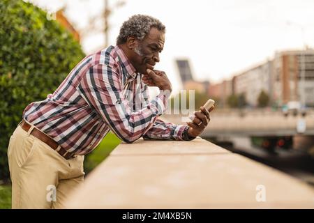 Thoughtful man using smart phone leaning on wall Stock Photo