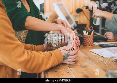 Couple putting mason jars in mesh bag at checkout counter in zero waste shop Stock Photo