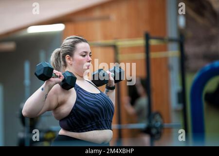 Overweight woman doing exercise with dumbbells in gym Stock Photo
