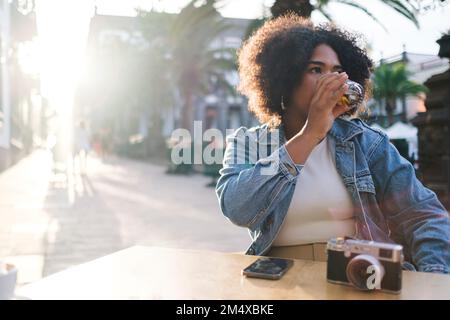 Young tourist having drink with camera on table at cafe Stock Photo