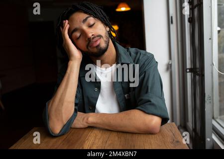 Tired man leaning on elbow at table near window in home Stock Photo