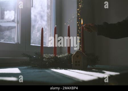 Woman burning candle on fir wreath at home in Christmas Stock Photo