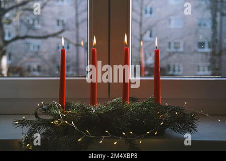 Burning red candles on advent wreath in front of window at home Stock Photo