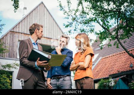 Couple discussing over documents with real estate agent in front of house Stock Photo