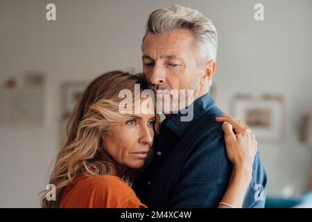 Thoughtful mature woman hugging man at home Stock Photo