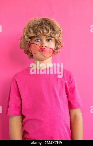Boy with colored sunglasses against pink background Stock Photo