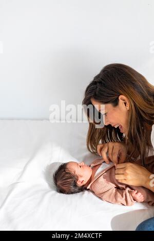 Mother playing with newborn daughter lying on bed at home Stock Photo
