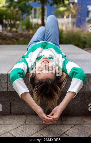 Happy young woman lying on concrete bench Stock Photo