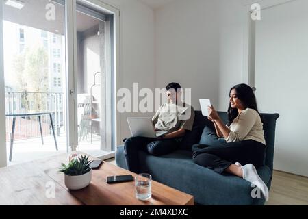 Young man and woman studying using laptop and tablet PC on sofa in living room Stock Photo