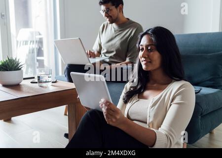 Young woman studying through tablet PC with man in background at home Stock Photo