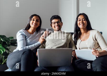 Smiling women and man with laptop and digital tablet sitting on sofa Stock Photo