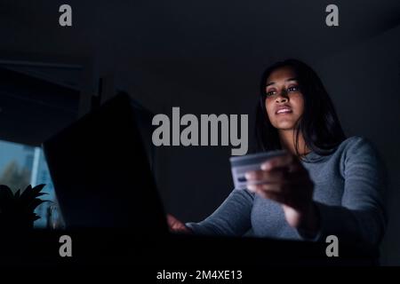 Young woman holding credit card doing online shopping through laptop at home Stock Photo