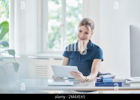 Happy female doctor using digital tablet PC at desk Stock Photo