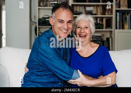 Smiling son embracing happy mother on sofa at home Stock Photo