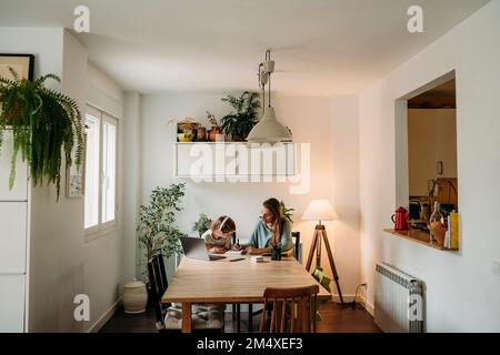 Mother explaining daughter sitting with laptop at table at home Stock Photo