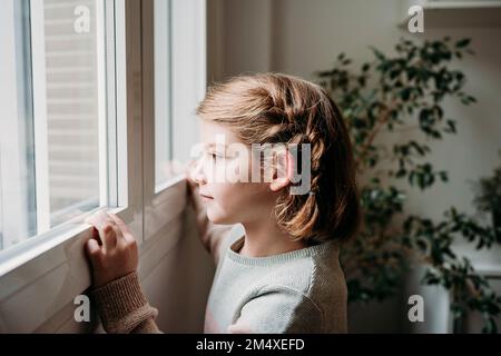 Thoughtful girl looking through window at home Stock Photo