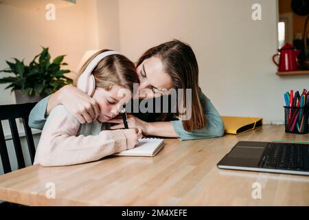 Mother kissing daughter doing homework at table at home Stock Photo