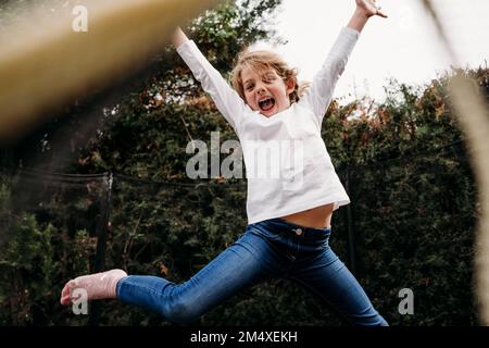 Playful girl with arms raised jumping in garden Stock Photo