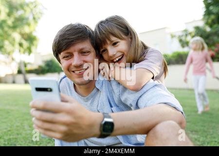 Happy daughter with father using smart phone in park Stock Photo