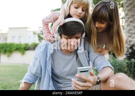 Happy father using smart phone with daughters in park Stock Photo