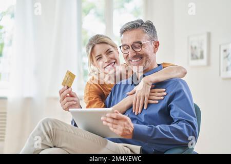 Happy woman embracing man with credit card doing online shopping through tablet PC at home Stock Photo