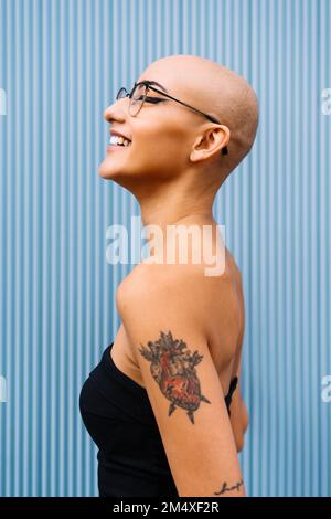 Happy woman with shaved head by blue wall Stock Photo