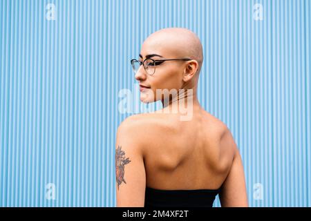 Woman with shaved head in front of blue wall Stock Photo