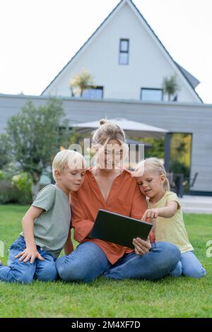 Happy mother sharing tablet PC with children in garden Stock Photo