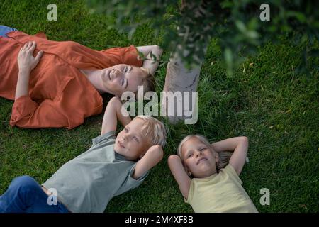 Smiling mother with children resting on grass in back yard Stock Photo