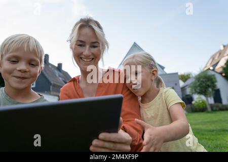 Happy woman sharing tablet PC with children in back yard Stock Photo