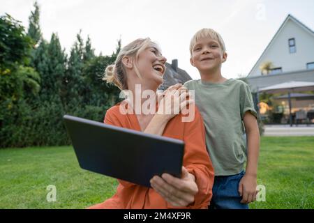 Happy mother with tablet PC looking at smiling son in garden Stock Photo