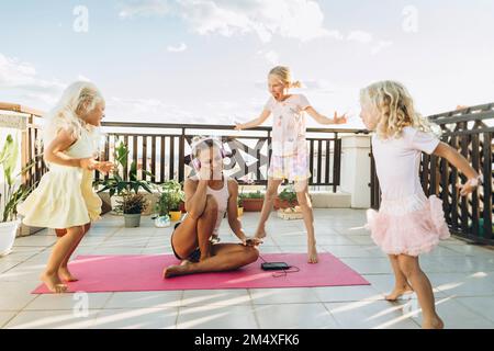 Girls romping around annoyed mother on roof terrace Stock Photo