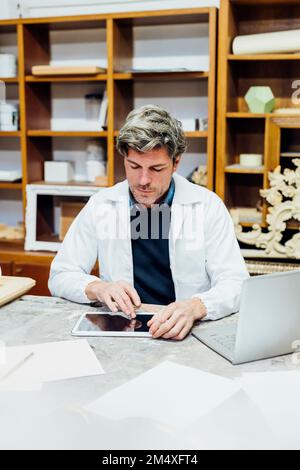 Craftsman wearing lab coat using tablet PC in workshop Stock Photo