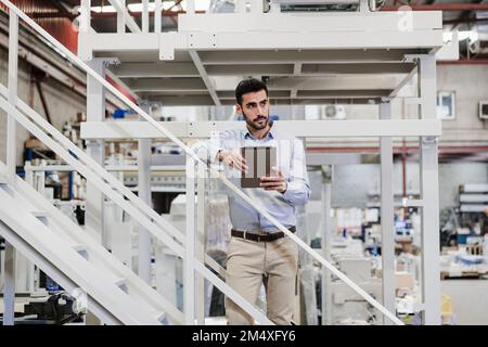 Contemplative businessman standing with tablet PC on staircase Stock Photo