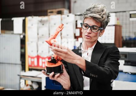 Mature businesswoman examining robotic arm in industry Stock Photo