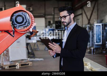 Engineer using tablet PC standing by robotic arm in industry Stock Photo